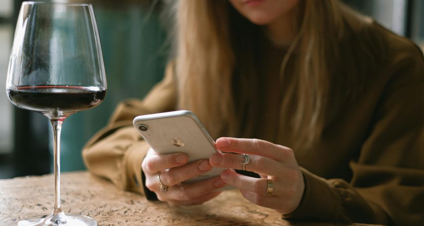 Woman Sitting with a Glass of Wine Scrolling Through Her Phone
