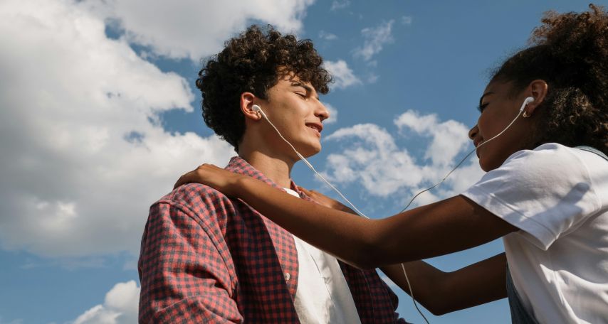 Teenage couple sharing headphones against blue sky